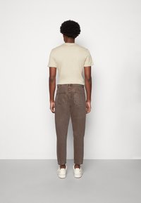 T-shirt beige en coton à manches courtes associée à un jean en denim marron taille haute. Le jean présente des jambes fuselées et est porté avec des baskets blanches.