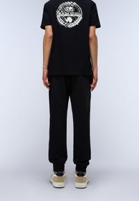 Black cotton t-shirt with a circular logo on the back, paired with black jogger pants and beige sneakers with dark accents. Simple design.