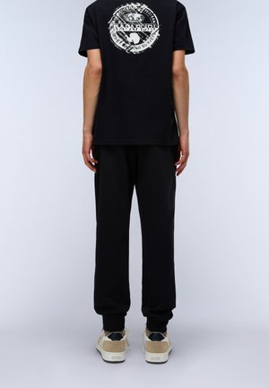 Black cotton t-shirt with a circular logo on the back, paired with black jogger pants and beige sneakers with dark accents. Simple design.