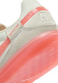 Baskets Nike avec un dessus en gris clair, une semelle intermédiaire rose texturée et une semelle extérieure rose translucide avec un design de grip motif.
