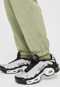 Nike Air Max sportcipők fekete és fehér dizájnnal, texturált felsőrésszel, légpárnázott talppal és gumitalppal, zöld joggerek mellett.