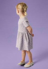 Vaaleanlila mekko lyhyillä hihoilla ja kukkakuoseilla, vyötäröltä kireä, yhdistettynä harmaisiin kenkiin, joissa on ristikkäiset hihnat.