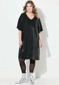 Vestido negro de lentejuelas con escote en V y mangas cortas y anchas. Combinado con medias negras y botines plateados, que presentan una textura suave y brillante.