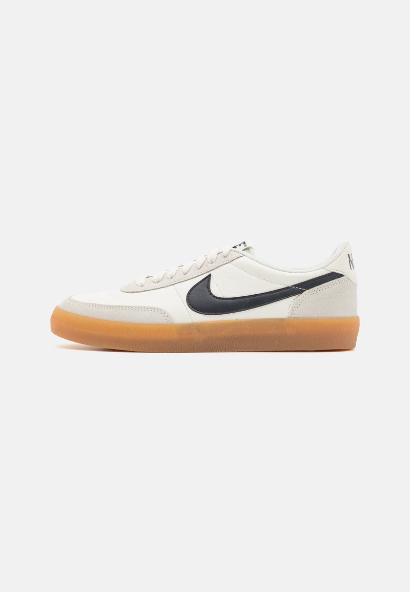 Bijeli tenisici s crnim Nike Swoosh-om, gumiranim potplatom i teksturiranim kožnim gornjim dijelom. Ima vezanje na vezice i podstavljeni ovratnik.