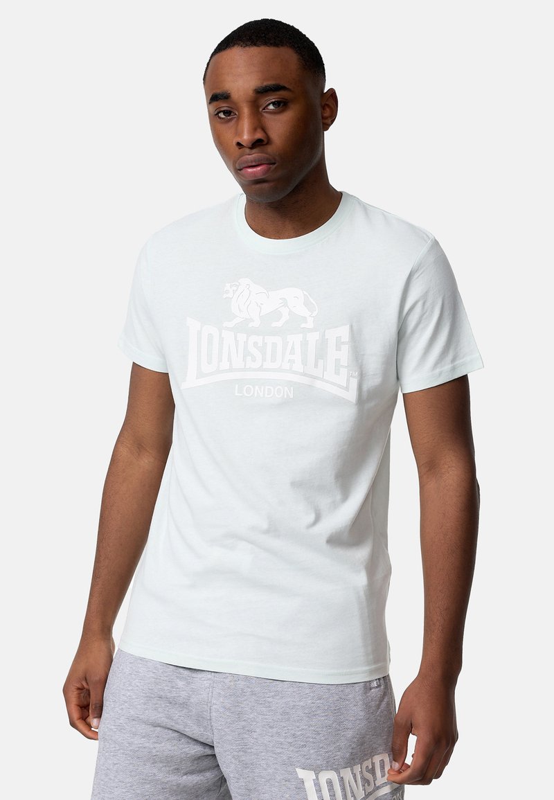 Camiseta de algodón de color azul claro con un estampado blanco del logo "LONSDALE LONDON" y un gráfico de león en el frente. Cuello redondo y mangas cortas.