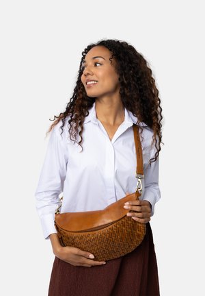 Borsa a spalla in pelle marrone chiaro con texture intrecciata, forma curvata, chiusura con zip e tracolla regolabile. Il modello indossa una camicia bianca e una gonna marrone.