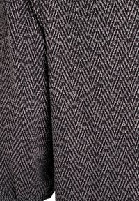 Juodas audinys su žuvų kaulų raštu, kuriame subtilūs metaliniai siūlai suteikia tekstūrą ir dizaino detales. Lygus ir vienodas paviršius.