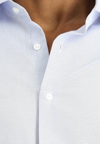 Lichtblauw overhemd met knopen en een klein ruitpatroon, met witte knopen en een gekraagde halslijn. Gestructureerde stof.