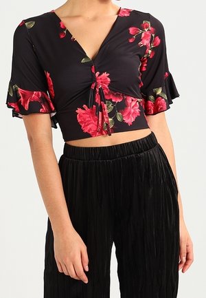 Haut court noir à imprimé floral rouge avec manches courtes volantées, associé à un pantalon noir plissé taille haute sur une personne.