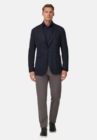 Granatowy blazer z teksturowanej tkaniny, z dwoma przednimi kieszeniami i klapą, w zestawie z jasnoszarymi spodniami i czarnymi sneakerami.