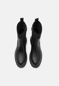 Botas negras hasta el tobillo con un exterior de cuero suave, paneles laterales elásticos y una suela de goma texturizada, con un cierre de cremallera en un lado.