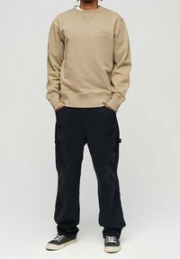 Felpa beige con collo rotondo e polsini a costine, abbinata a pantaloni in velluto a costina blu scuro a vestibilità morbida e sneakers nere.