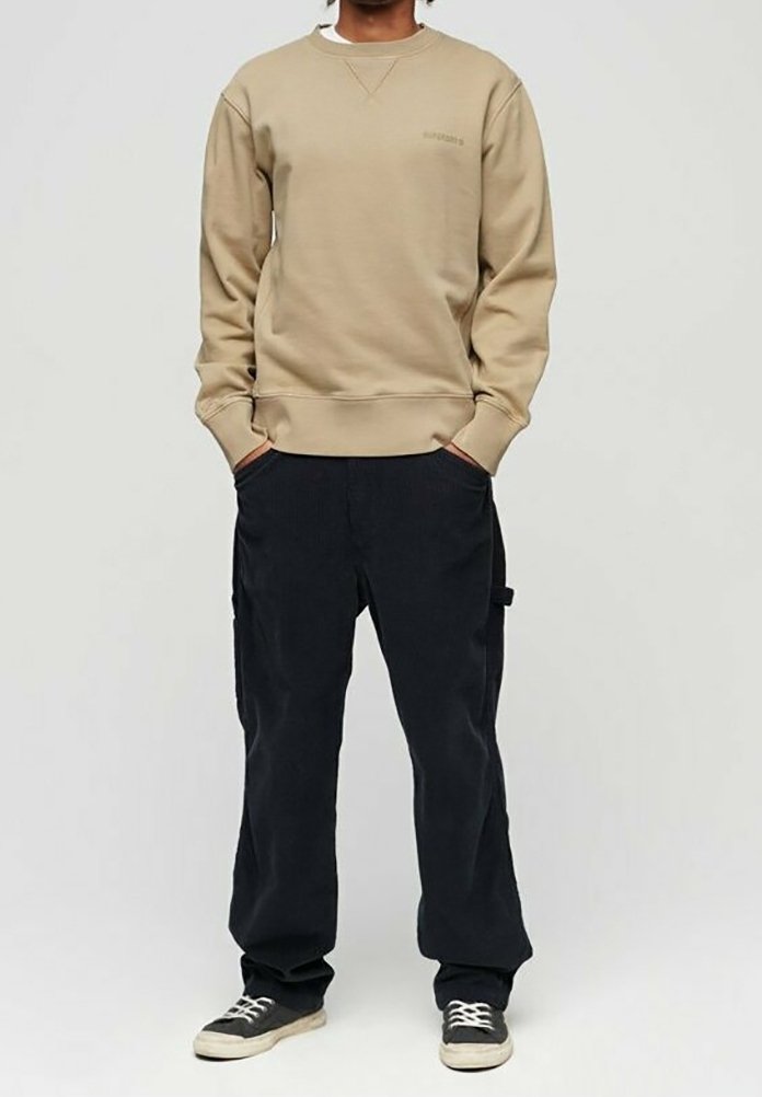 Felpa beige con collo rotondo e polsini a costine, abbinata a pantaloni in velluto a costina blu scuro a vestibilità morbida e sneakers nere.