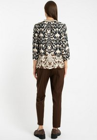 Długi rękaw bluzka z kontrastowym wzorem damaskowym w kolorze granatowym i beżowym; zestawiona z brązowymi spodniami i brązowymi masywnymi butami.