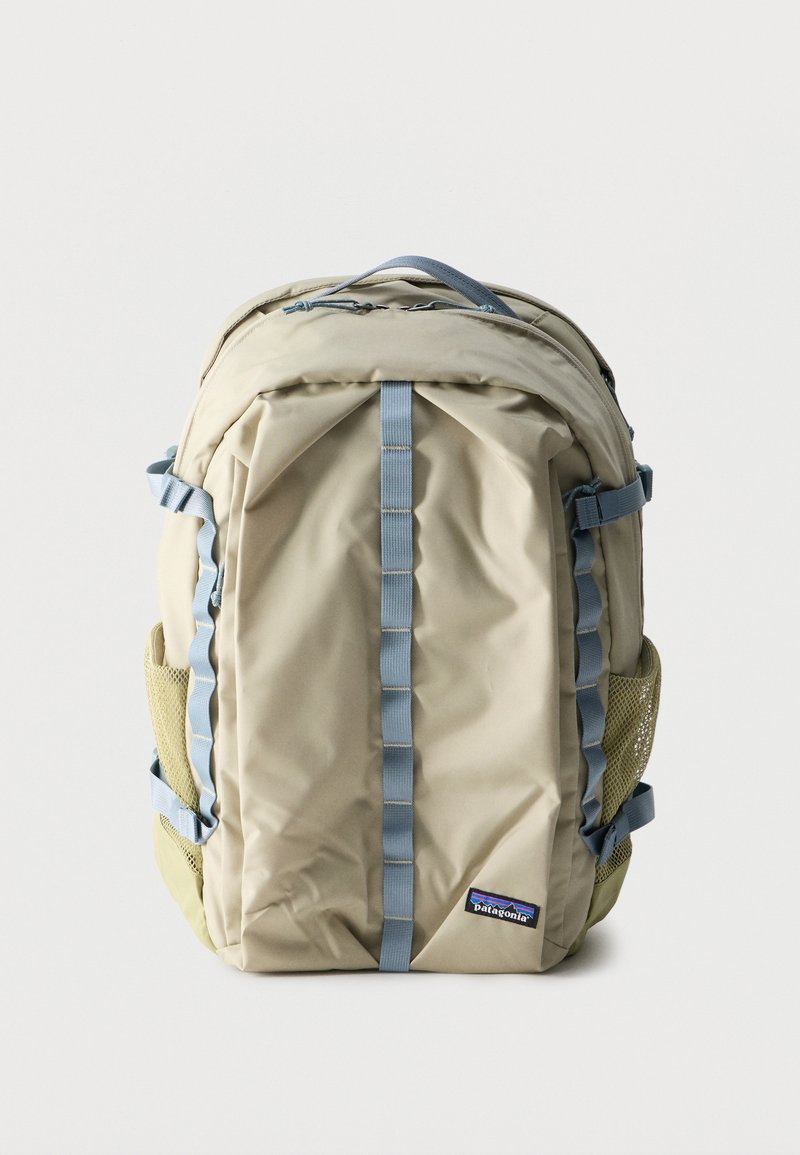 Μπεζ σακίδιο πλάτης Patagonia με μπλε ιμάντες, δίχτυα πλαϊνές τσέπες, κορυφαία λαβή και μπροστινό λογότυπο, απεικονίζεται όρθιο σε λευκό φόντο.