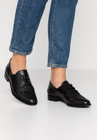 Chaussures en cuir noir avec un motif tissé sur le bout, design à lacets et petit talon, associées à un pantalon en denim bleu cropped.