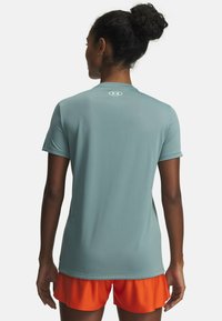 Korte mouwen sportshirt van lichtblauwe stof, voorzien van een ronde halslijn en een klein logo op de achterkant. Gecombineerd met oranje shorts.