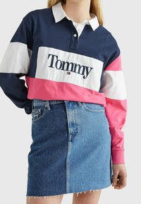 Langärmliges Rugby-Shirt in Marineblau, Weiß und Pink mit Kragen und "Tommy"-Logo. Kombiniert mit einem blauen Jeansrock mit fransigem Saum.