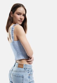 Blå smocket crop-top med rynkede hvide stropper; parret med lyse denim jeans med et brunt læderpatch på baglommen.