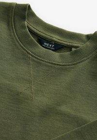 Olivgrön sweatshirt med ribbad halsringning, texturerat tyg och synliga sömnadsdetaljer. Etiketten visar "NEXT" och "Tillverkad i Bangladesh."
