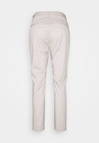 Pantalon beige droit avec deux poches passepoilées à l'arrière et passants de ceinture, vu de dos sur un fond uni.