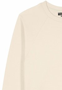 Light beige sweatshirt with a round neckline, raglan sleeves, and soft texture. Features a label with the brand name at the collar.