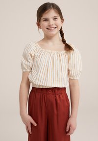 Blusa bianca con strisce verticali dorate, maniche a sbuffo e scollatura quadrata, abbinata a pantaloni rustico con vita alta e bottone.