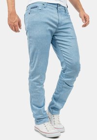 Lichtblauwe denimjeans met een gestructureerde afwerking, slanke pasvorm, voor- en achterzakken en zilverkleurige hardware. Draag je met witte sneakers.
