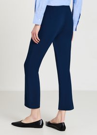 Pantalons tailleur bleu marine à jambe droite, en tissu lisse, associés à des chaussures plates noires, vus de l'arrière.