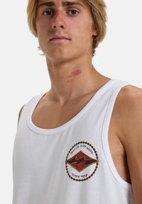 White cotton tank top featuring a colorful embroidered logo with red and yellow accents inside a circular design. Simple neckline, relaxed fit.