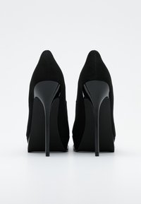 Svarta högklackade skor med en stilren, spetsig tådesign. Tillverkade av strukturerad textil med glänsande, böjda klackar.