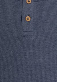 Polo shirt a coste di colore blu navy con un colletto ordinato e un'apertura a tre bottoni con bottoni marrone chiaro.