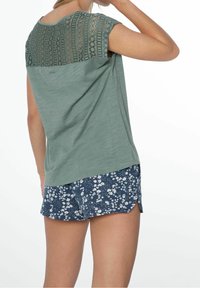 Kortærmet, grøn top med blonde detaljer bagpå, parret med blå mønstrede shorts med hvide blomsterdesigns og en afslappet pasform.