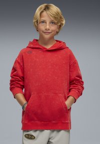 Czerwona bluza z kapturem o wyblakłej fakturze i przedniej kieszeni. Posiada ribbowe mankiety i logo na piersi. Luźny krój, wykonana z miękkiego materiału.