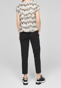 Top a maniche corte con un motivo bianco e marrone, abbinato a pantaloni neri a sigaretta e sneakers nere con un accento lucido.