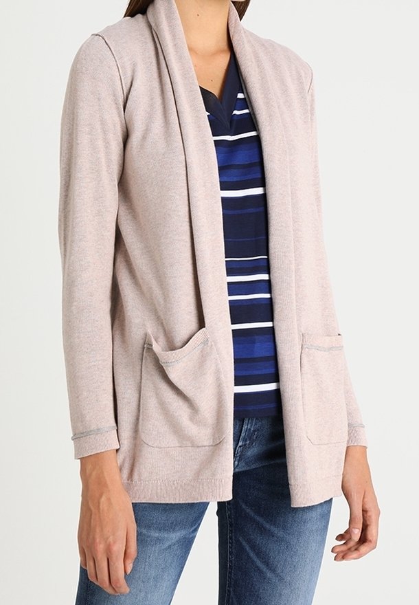 Žena v svetle růžovém cardiganě s otevřeným předním dílem a dvěma předními kapsami, pod ním má modro-bíle pruhované tričko a modré džíny.