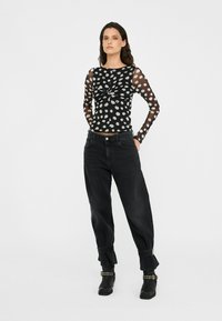 Top in rete nero con pois, maniche lunghe e dettaglio annodato nella parte anteriore; abbinato a jeans neri a vita alta e stivaletti con tacco e borchie.
