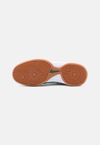 Nike sneakers zole ar baltu teksturētu pamatni un brūnu gumijas ārējo slāni, kurā ir apļveida un zigzaga tread raksti un zaļš logotipa akcents.