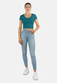 Türkisfarbenes, kurzes T-Shirt mit kurzen Ärmeln, kombiniert mit hellblauen, hochgeschnittenen Jeans und weißen Sneakers. Einfaches Design, keine Muster.