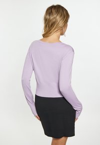 Pulover tricotat lila cu mâneci lungi, design ajustat și spate decupat, asortat cu o fustă neagră cu un tiv crestat.