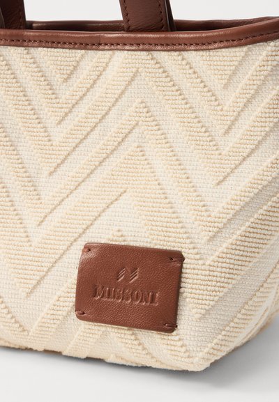 Sac fourre-tout en beige texturé présentant un motif en chevrons et des accents en cuir marron, y compris une étiquette de logo. Poignées robustes en marron.