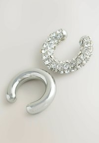 To sølvfarvede krogformede accessories: den ene glat og skinnende, den anden prydet med klare rhinsten og har et buet design.