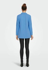 Blazer azul de manga larga con una silueta ajustada, hecho de tela suave, combinado con leggings de cuero negro y botas negras de tobillo.
