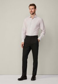 Camisa de vestir a rayas en rosa claro, pantalones de vestir negros y zapatos negros. Diseño ajustado, camisa con botones y sutil textura en la tela.