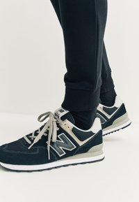 Zwart-grijze New Balance sneakers met een mesh en suède bovenwerk, platte veters, rubberen zool en het "N"-logo aan de zijkant.