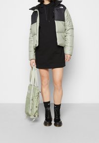 Jasnozielona kurtka puchowa z czarnymi ramionami, czarna sukienka z kapturem, zielony plecak, czarne sznurowane botki i czarne skarpetki.