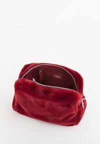 Bolsa de cosméticos de piel sintética roja con forma rectangular y cierre de cremallera en la parte superior. El interior cuenta con un pequeño bolsillo con cremallera y una etiqueta con la marca.