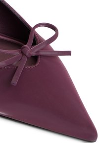 Violetti kiiltonahka flatsit, joissa on teräväkärkinen muotoilu, etuosassa koristeena suloinen nauha ja sileä pinta. Sivussa näkyvillä leikkaukset.
