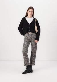 Cardigan nero corto con chiusura a bottoni, t-shirt bianca sotto, pantaloni in stampa serpente e stivaletti neri. Borsa beige con tracolla.