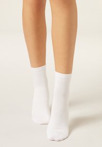 Weiße Baumwoll-Knöchelsocken mit einem gerippten Bund, glatter Textur und nahtloser Zehenpartie, die knapp über dem Knöchel sitzen.